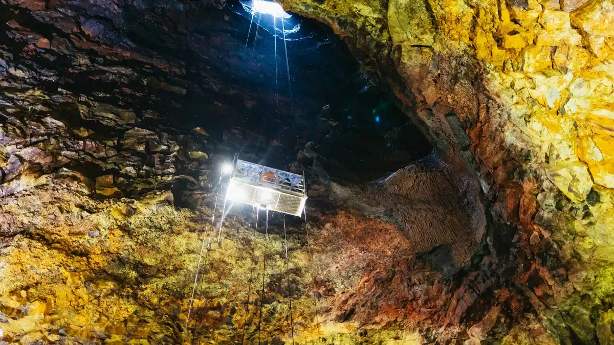 Visitors in helmets on the open lift descending into the rust-red magma chamber on a Thrihnukagigur volcano tour in Bláfjöll, Iceland